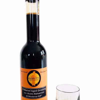 One 8.8 oz bottle of Giannetti Artisans balsamic vinegar with a small glass of the actual vinegar next to the bottle on a whitel background