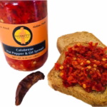 Close up of a 7 oz jar of Giannetti Artisans Italian Calabrese Hot Pepper Spread next to a piece of toast that displays the actual spread and a hot pepper in front of the jar