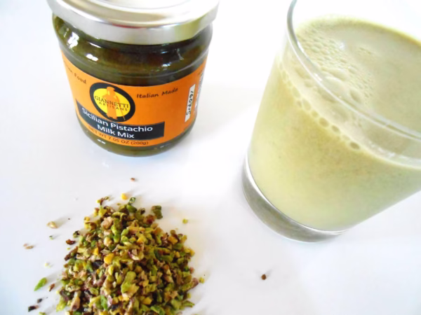 Top view of 7 oz Giannetti Artisans Pistachio Paste jar and a glass of the pistachio milk with pistachio grains on the side on a white background