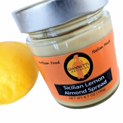 Top side view of a 7 oz Giannetti Artisans Lemon Almond Spread jar with a lemon prop on the side on a white background