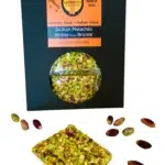 Front view of a black package of Giannetti Artisans Sicilian Pistachio Brittle with a piece of brittle and loose pistachios in front.