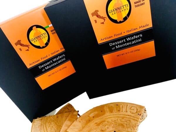 Two black packaging boxes of Giannetti Artisans montecatini wafers and pieces of wafer sitting in front of the boxes as prop on a white background