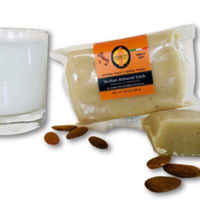 Front view of Giannetti Artisans Almond Paste in a brick form next to a glass of almond milk made from the almond paste surrounded by almonds on a white background