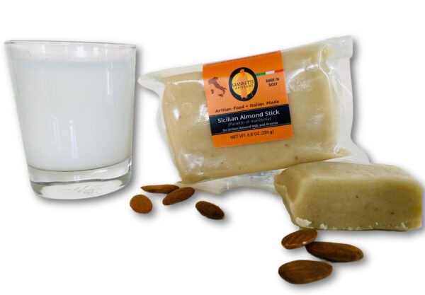 Front view of Giannetti Artisans Almond Paste in a brick form next to a glass of almond milk made from the almond paste surrounded by almonds on a white background